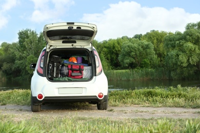 Photo of Car with camping equipment in trunk on riverbank. Space for text