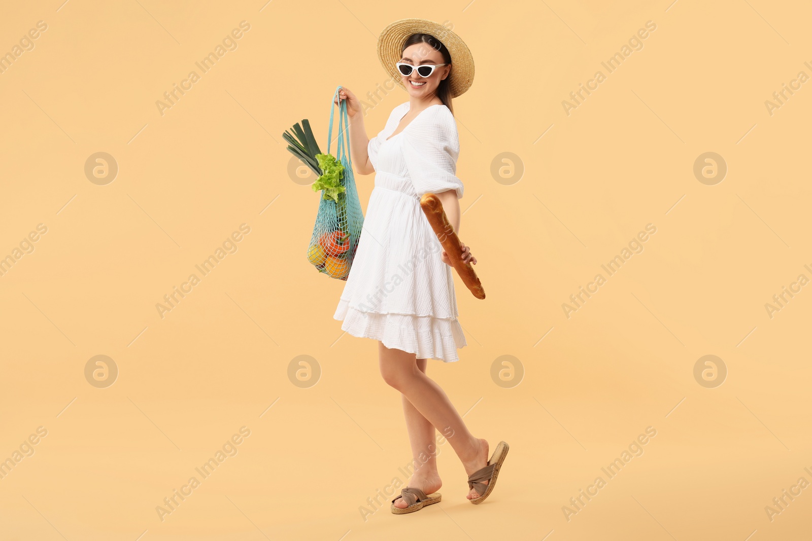 Photo of Woman with string bag of fresh vegetables and baguette on beige background