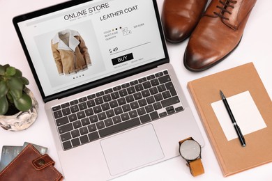 Photo of Online store website on laptop screen. Computer, stationery, credit cards, men's shoes and accessories on white background, above view