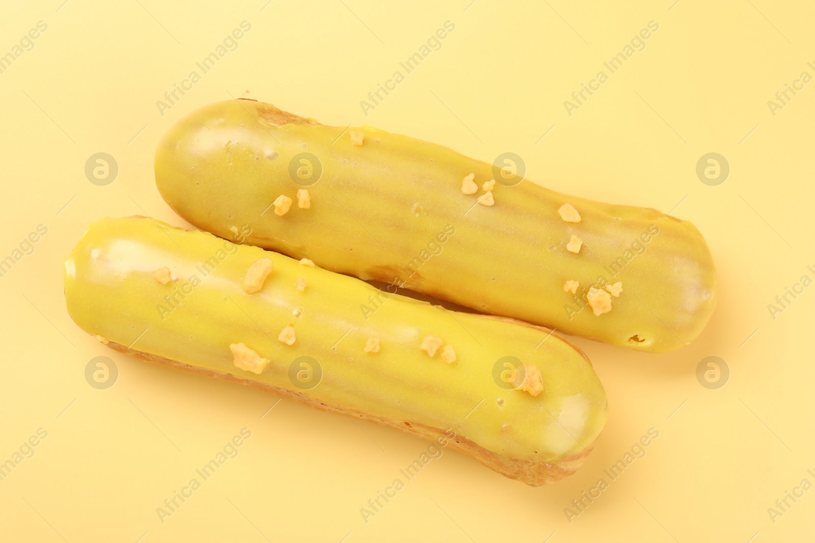 Photo of Delicious eclairs covered with glaze on yellow background, top view