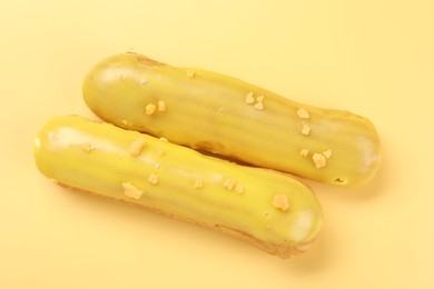 Photo of Delicious eclairs covered with glaze on yellow background, top view