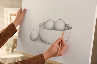 Woman drawing bowl of fruits with graphite pencil on canvas indoors, closeup