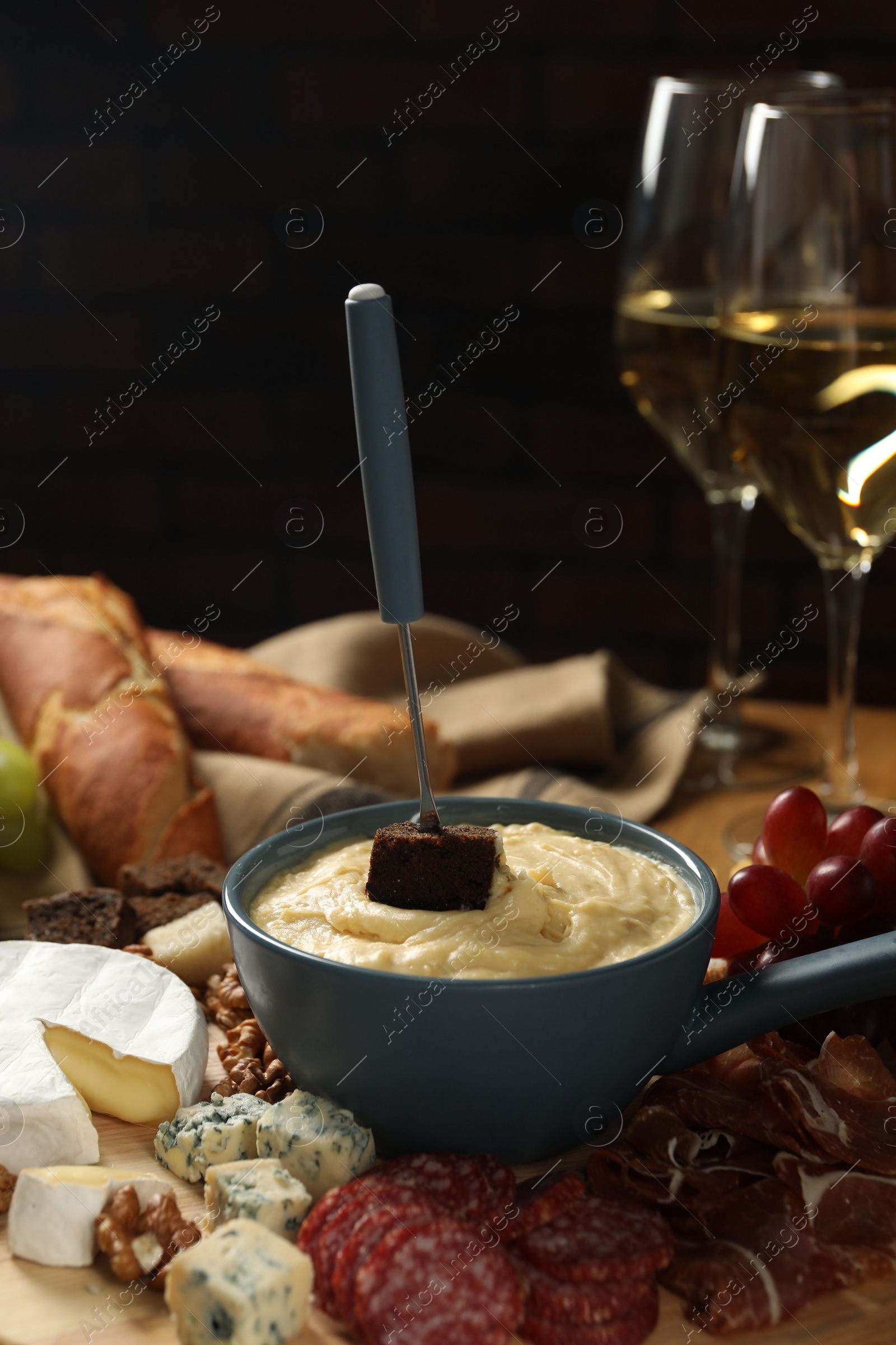 Photo of Fondue pot with tasty melted cheese, fork, different snacks and wine on table