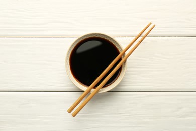 Photo of Tasty soy sauce in bowl and chopsticks on white wooden table, top view