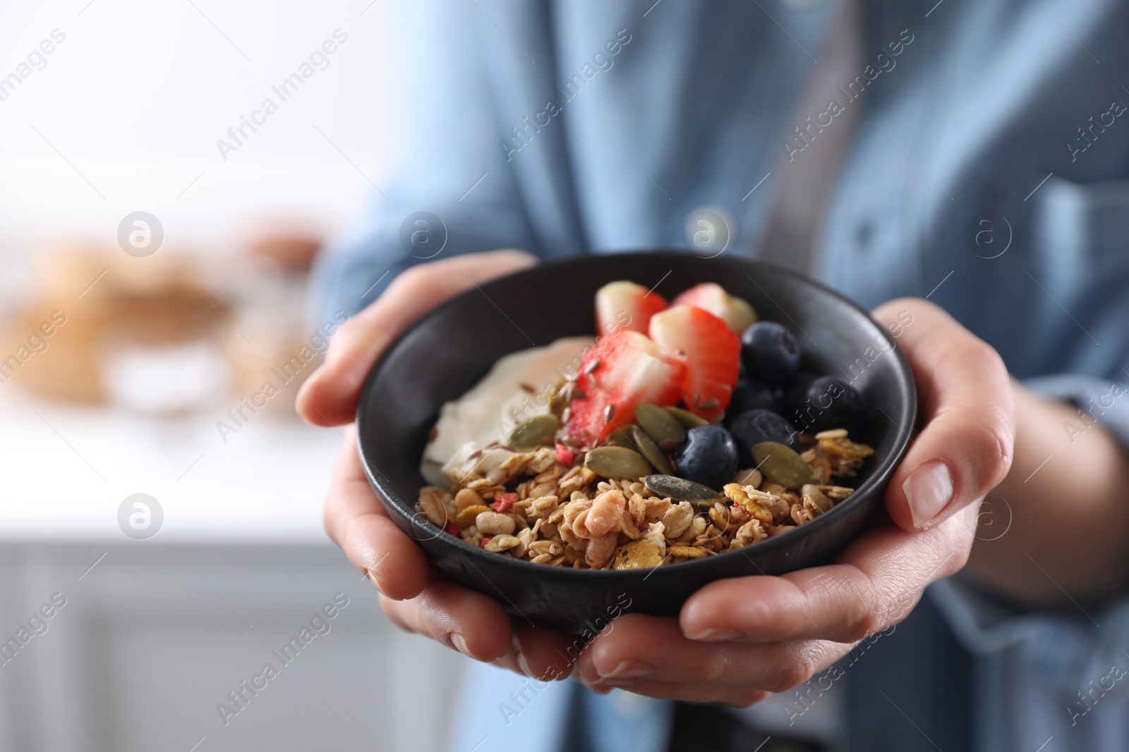 Photo of Woman holding bowl of tasty granola with berries, yogurt and seeds indoors, closeup