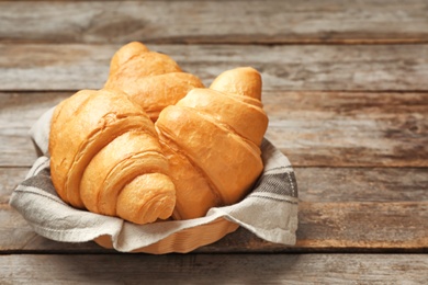Photo of Basket with tasty croissants on wooden table