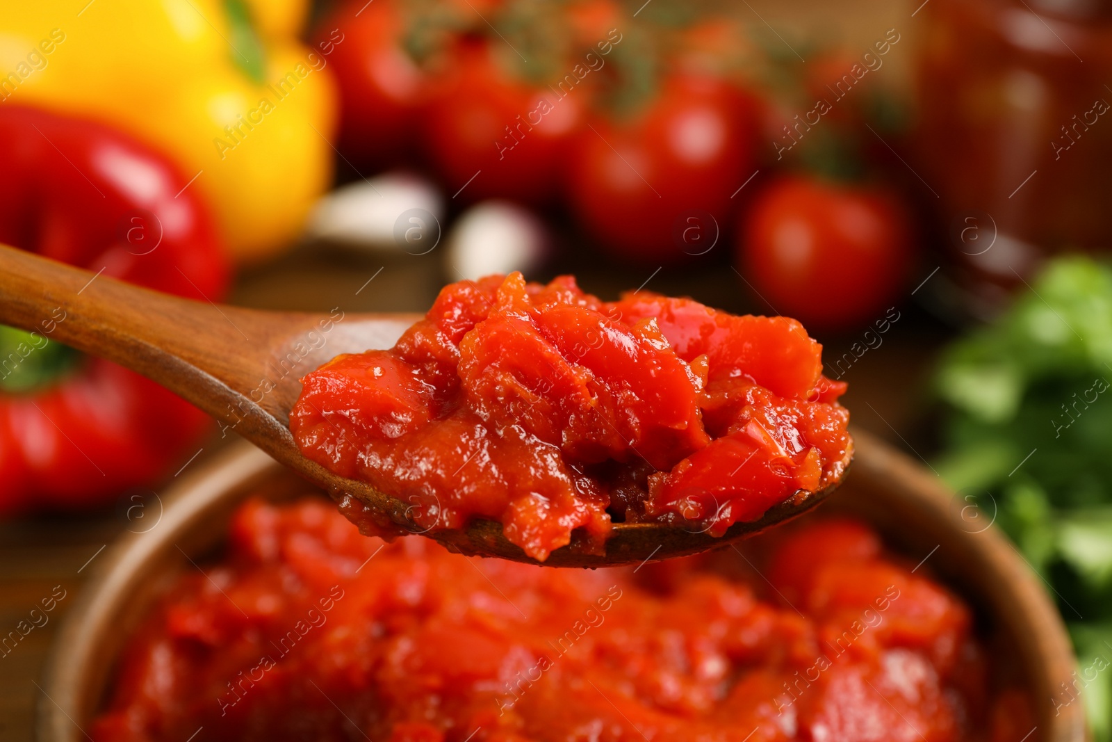 Photo of Wooden spoon with delicious lecho over bowl, closeup