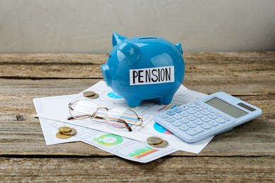 Piggy bank with word Pension, coins, glasses, calculator and diagrams on wooden table. Retirement savings