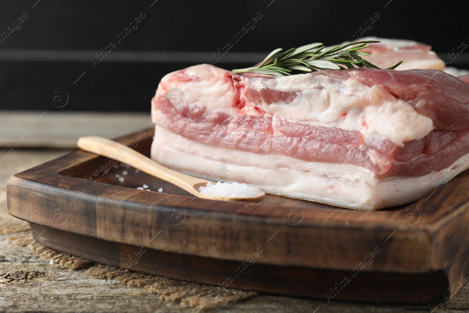 Photo of Piece of raw pork belly, salt and rosemary on wooden table, closeup