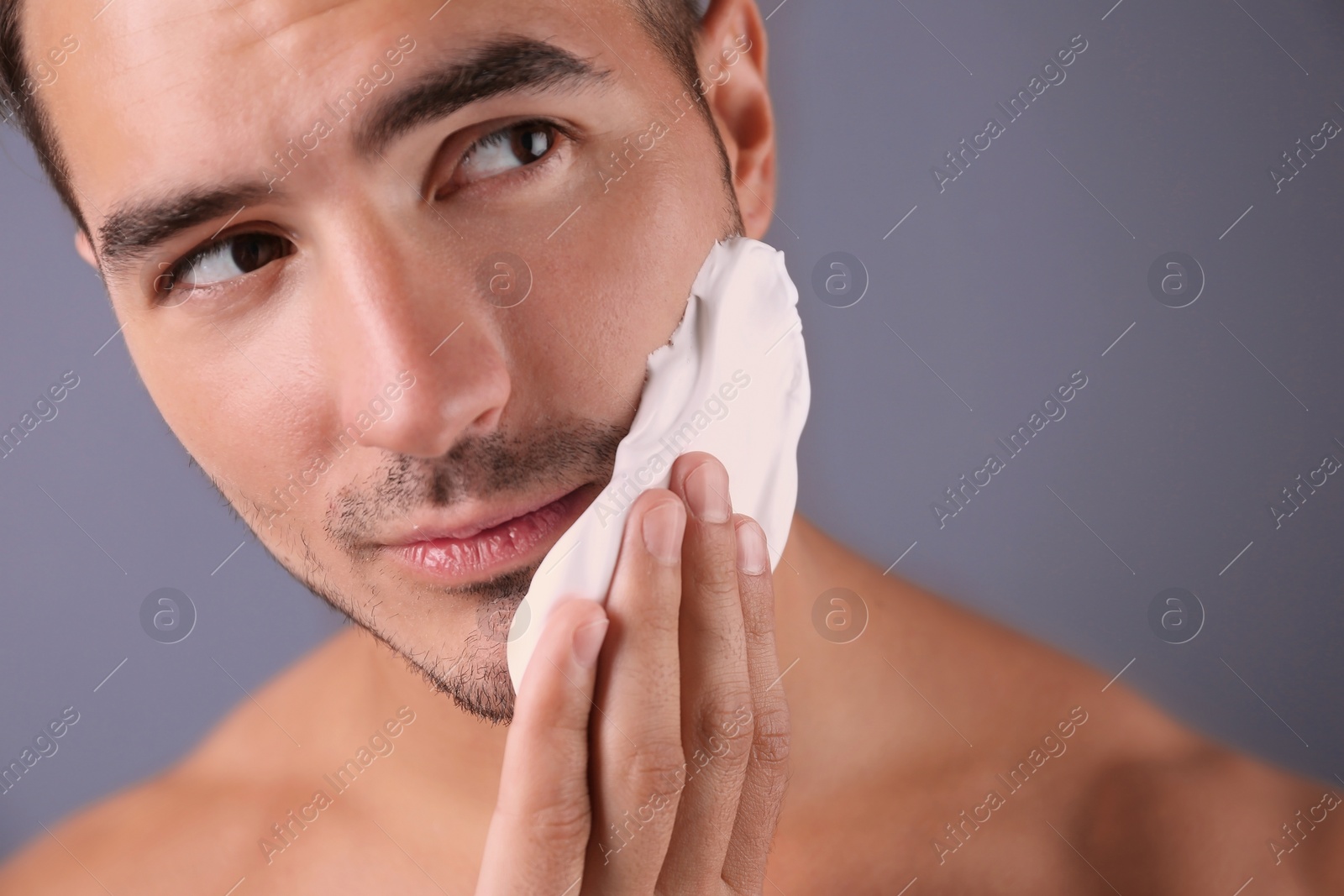 Photo of Handsome young man applying shaving foam on color background