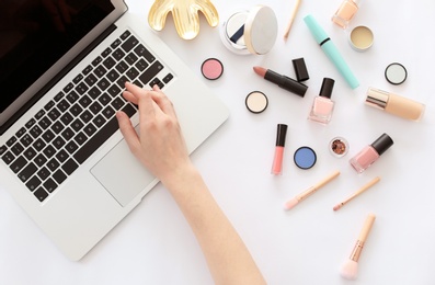 Young woman with makeup products using laptop at table. Beauty blogger