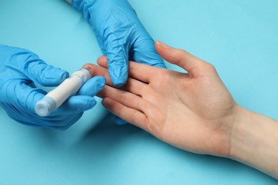 Diabetes. glucose testing. Doctor using lancet pen on light blue background, closeup