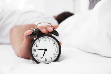 Man turning off alarm clock in bedroom