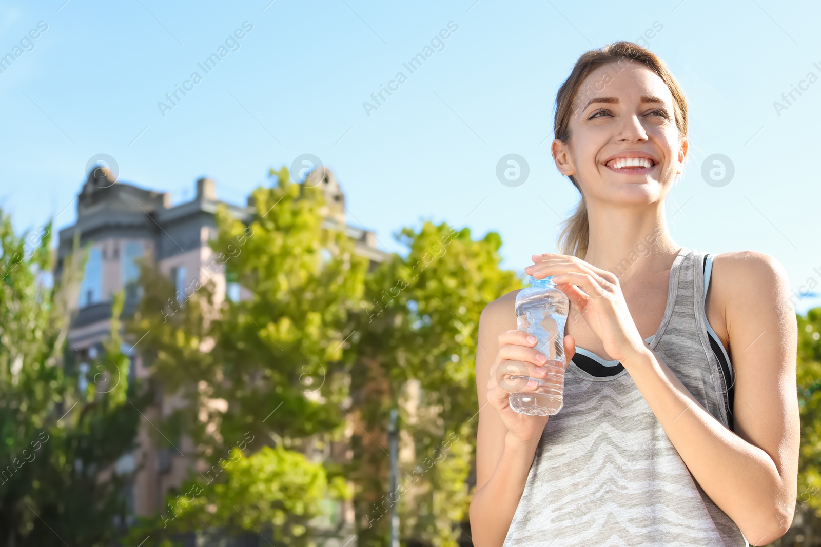 Photo of Young woman holding bottle with clean water on street. Space for text