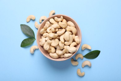 Photo of Many tasty cashew nuts and leaves on light blue background, top view