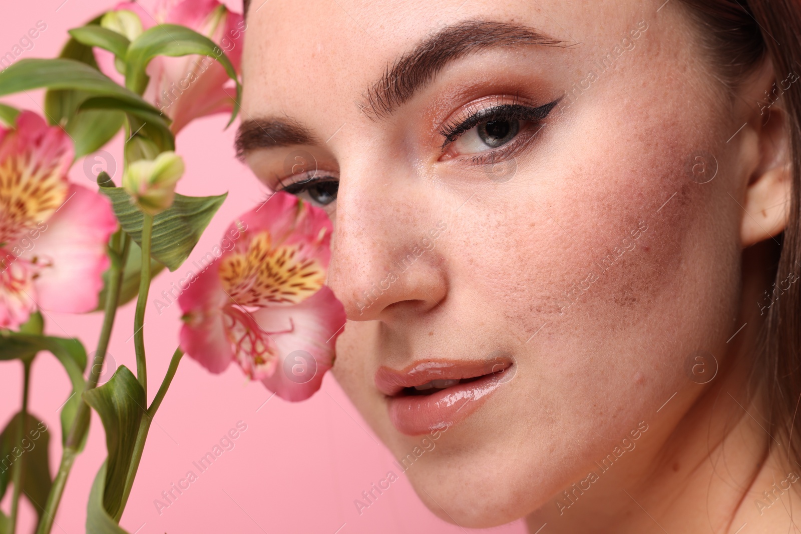 Photo of Beautiful woman with fake freckles and flowers on pink background, closeup