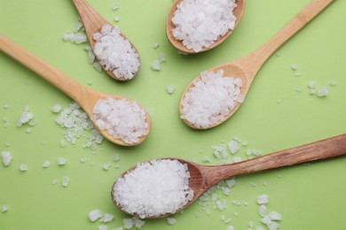 Photo of Spoons with sea salt on light green background, flat lay