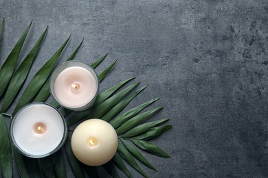 Burning wax candles and tropic leaf on grey background, top view