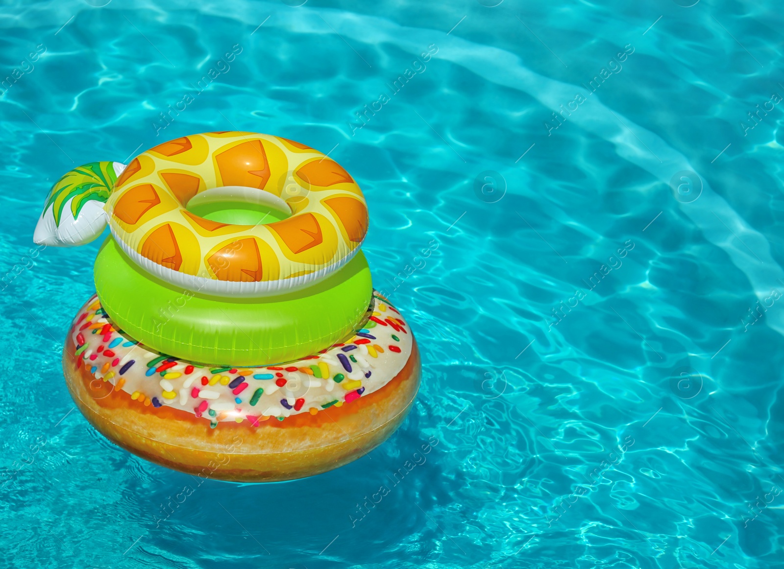 Photo of Stack of colorful inflatable rings floating in swimming pool on sunny day. Space for text