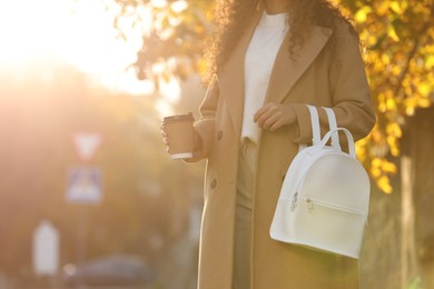 Photo of African-American woman with stylish white backpack and hot drink outdoors on sunny day, closeup. Space for text
