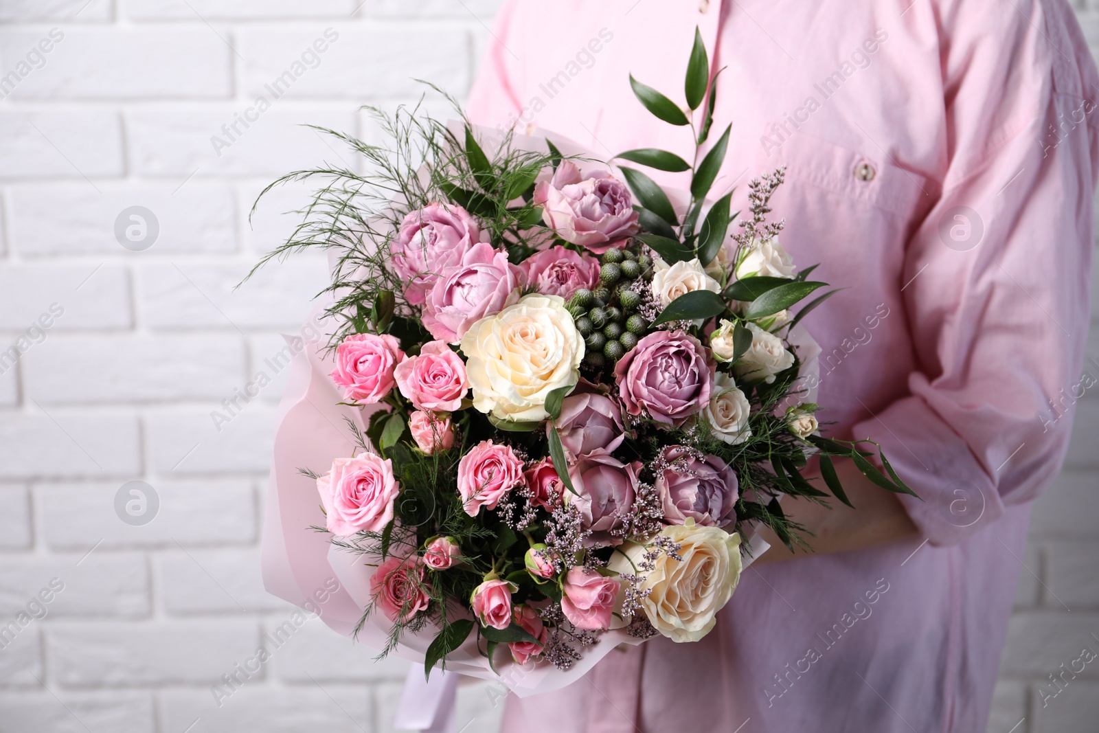 Photo of Woman with bouquet of beautiful roses near white brick wall, closeup