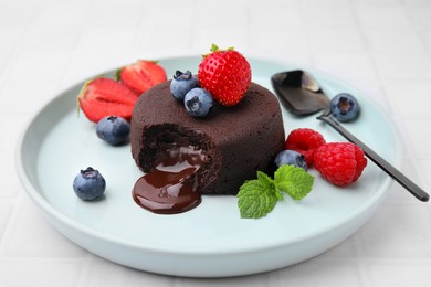 Photo of Plate with delicious chocolate fondant, berries and mint on white tiled table, closeup