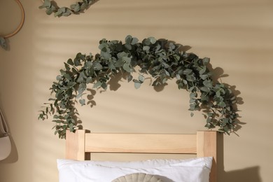 Photo of Beautiful garland made of eucalyptus branches hanging on light olive wall in bedroom