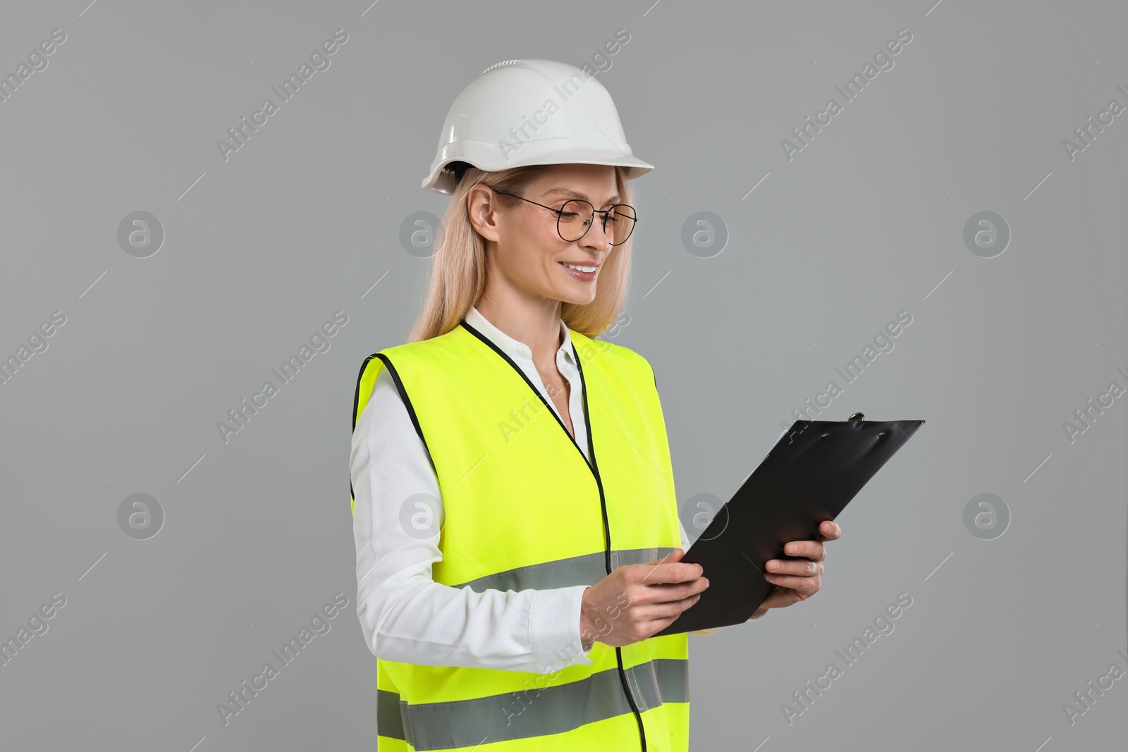 Photo of Engineer in hard hat holding clipboard on grey background