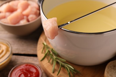 Photo of Fondue pot with oil, fork, raw meat pieces and other products on wooden table, closeup