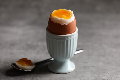 Photo of Cup with fresh soft boiled egg on grey table, closeup