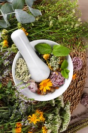 Mortar with pestle and many different herbs on table, flat lay