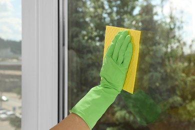 Photo of Woman cleaning window glass with sponge cloth indoors, closeup