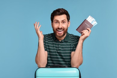 Happy man with passport, suitcase and tickets on light blue background