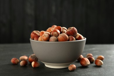 Photo of Ceramic bowl with hazelnuts on black table. Cooking utensil
