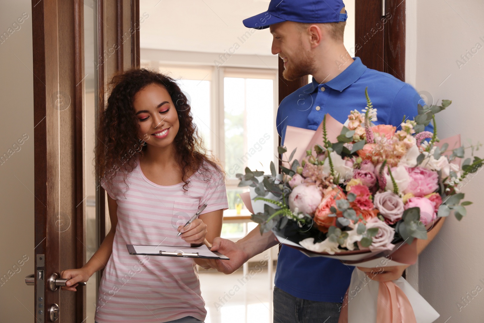 Photo of African-American woman receiving flower bouquet from delivery man indoors