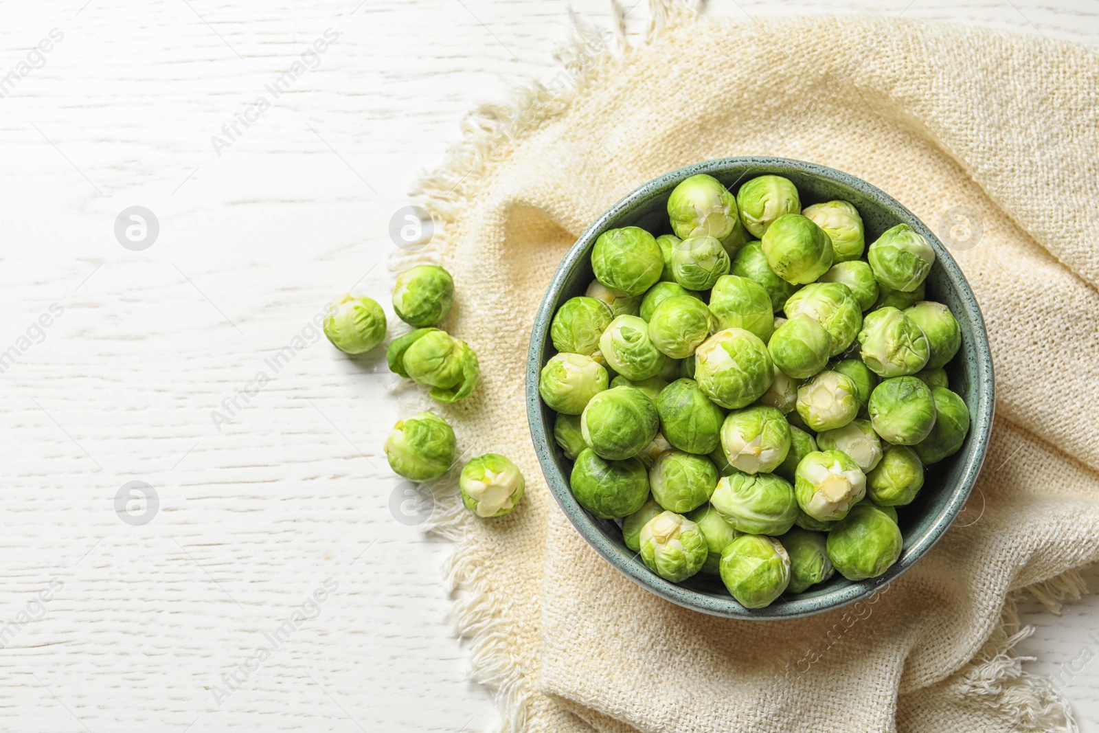 Photo of Bowl of fresh Brussels sprouts and napkin on wooden background, top view with space for text