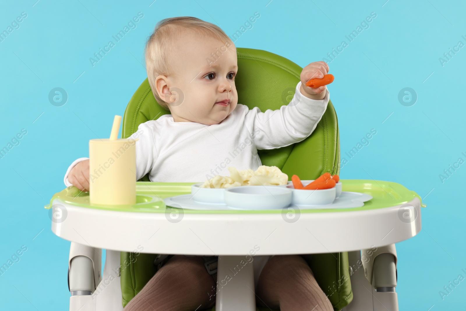 Photo of Cute little baby with healthy food in high chair on light blue background