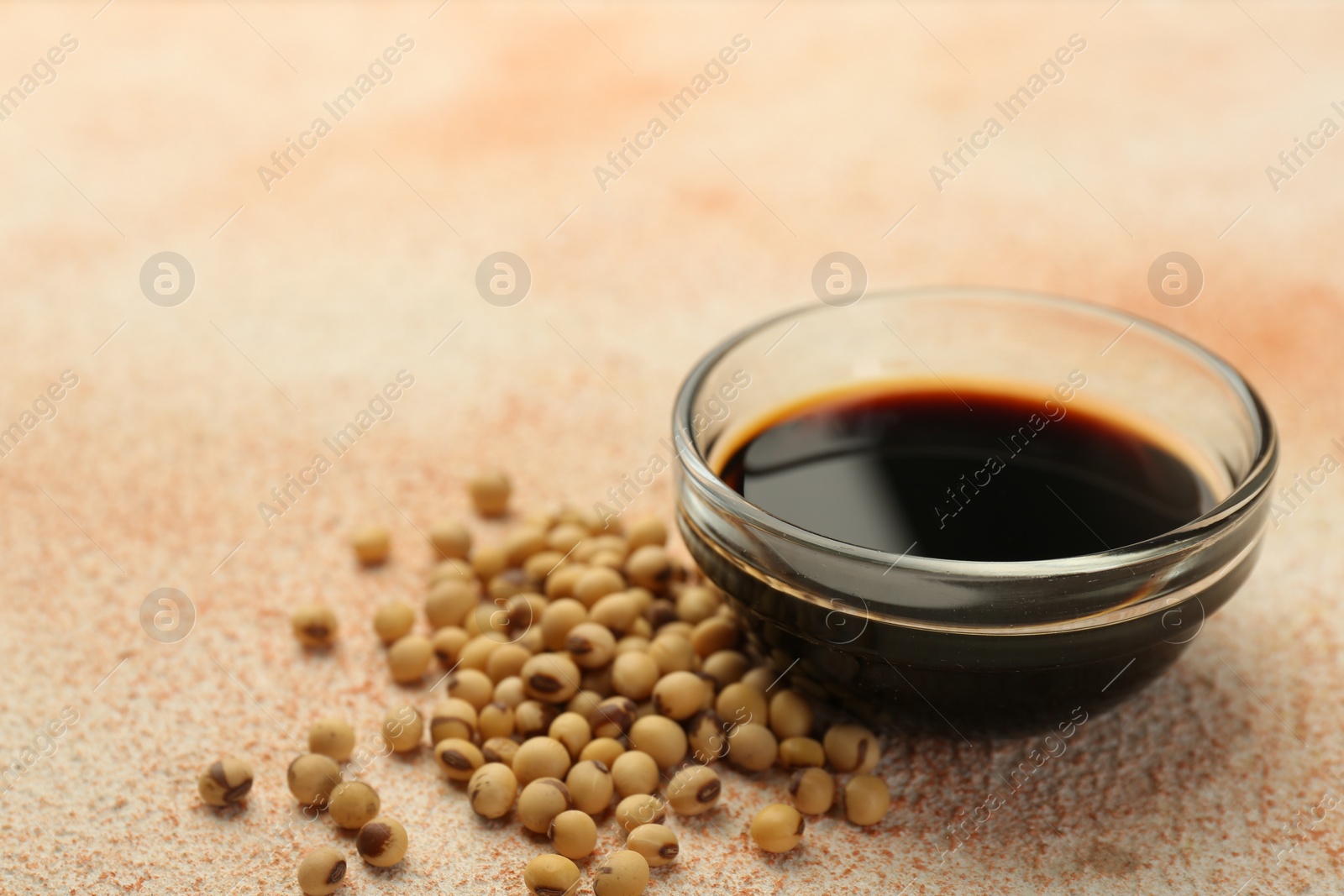 Photo of Soy sauce in bowl and beans on beige textured table, closeup. Space for text