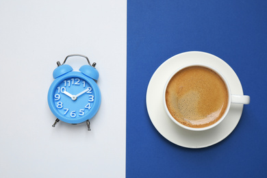 Photo of Black coffee and alarm clock on bright background, top view. Color of the year 2020 (Classic blue)