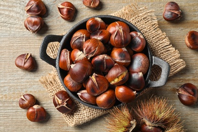 Photo of Tasty roasted edible chestnuts on wooden table, flat lay