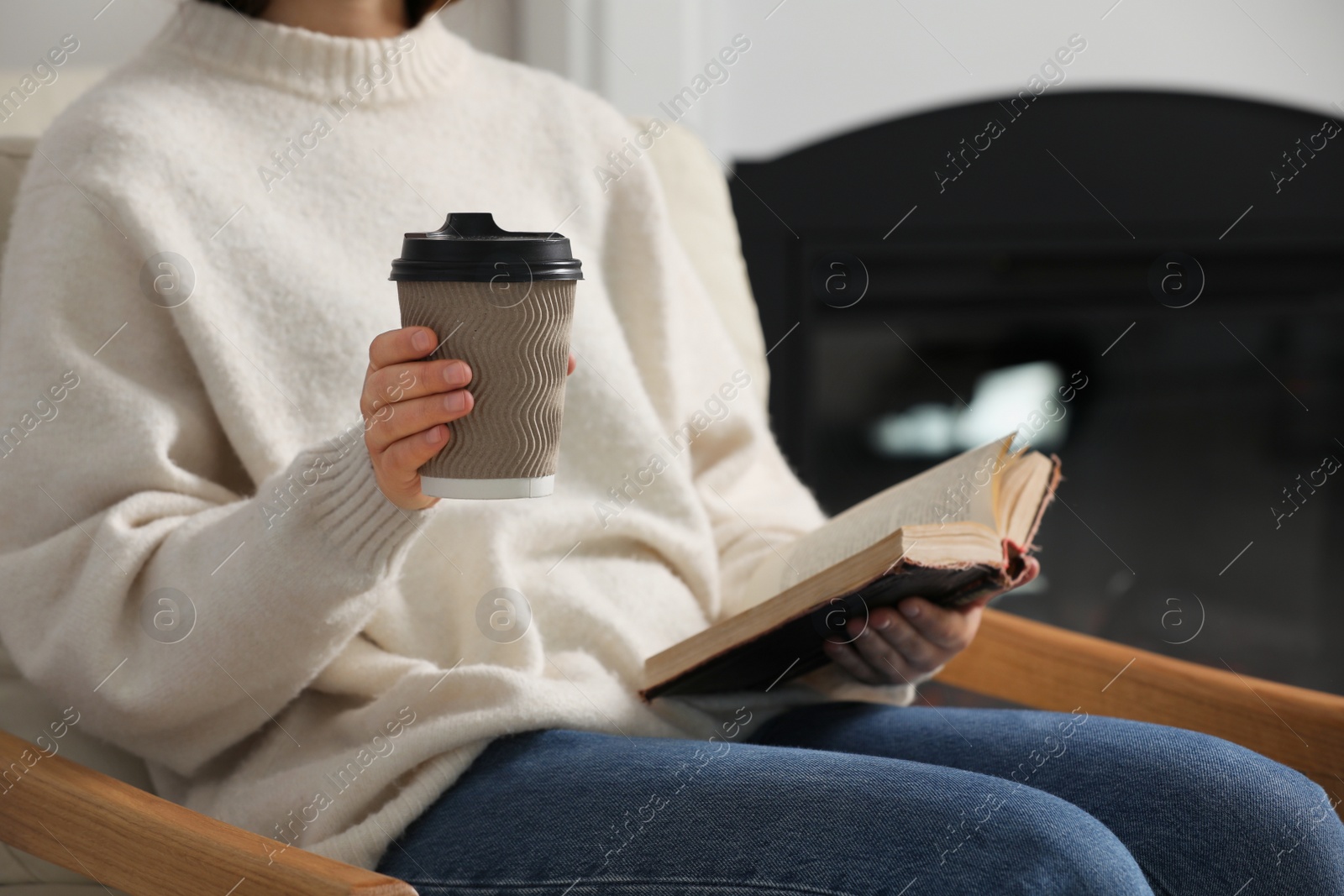 Photo of Woman holding takeaway cardboard cup and book indoors, closeup. Coffee to go