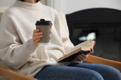 Woman holding takeaway cardboard cup and book indoors, closeup. Coffee to go