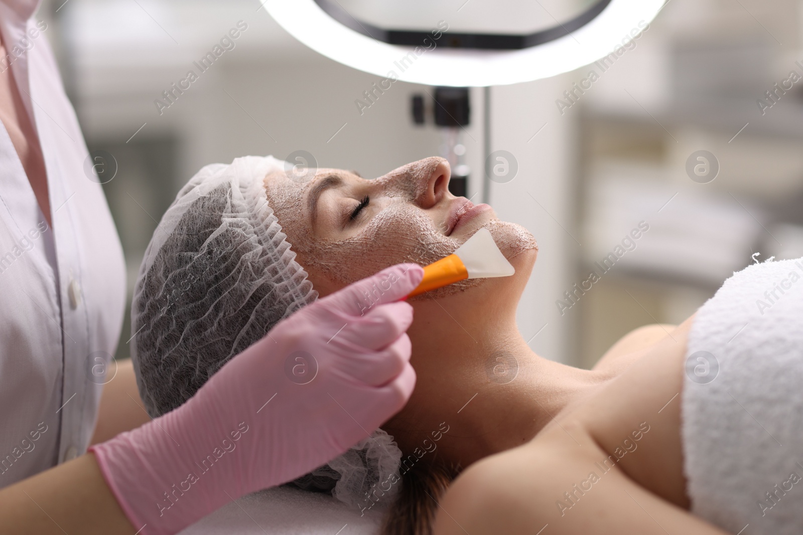 Photo of Cosmetologist applying mask on woman's face in clinic, closeup