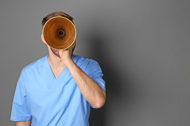 Male doctor with megaphone on grey background