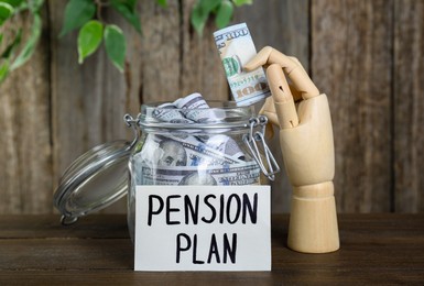 Photo of Card with phrase Pension Plan, mannequin hand and money in glass jar on wooden table. Retirement concept