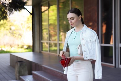 Photo of Young woman holding purse with credit card outdoors, space for text