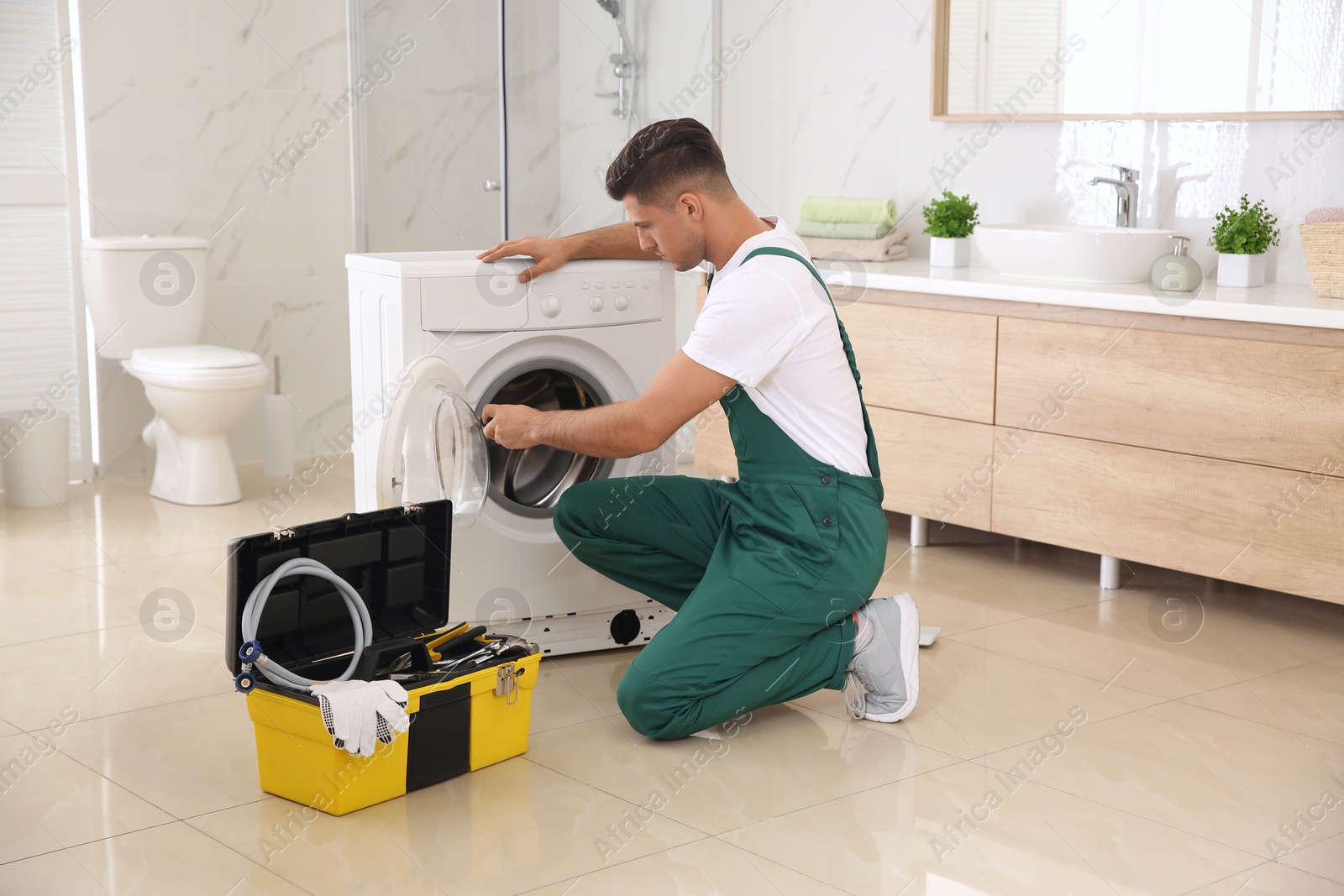 Photo of Professional plumber repairing washing machine in bathroom