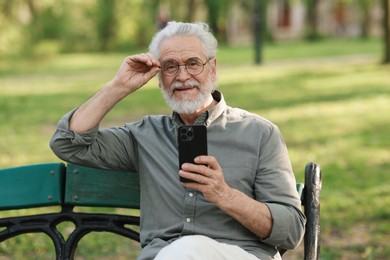 Portrait of happy grandpa with glasses using smartphone on bench in park