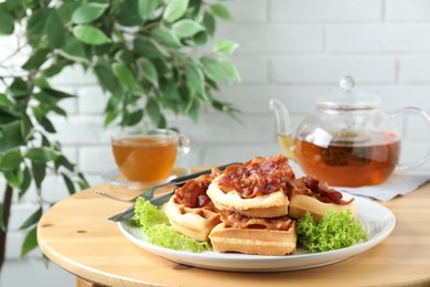 Tasty Belgian waffles served with bacon, lettuce and tea on wooden table