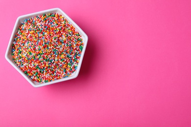 Photo of Colorful sprinkles in bowl on pink background, top view with space for text. Confectionery decor
